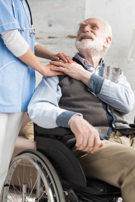 Doctor holding hands with cheerful and disabled senior man in wheelchair