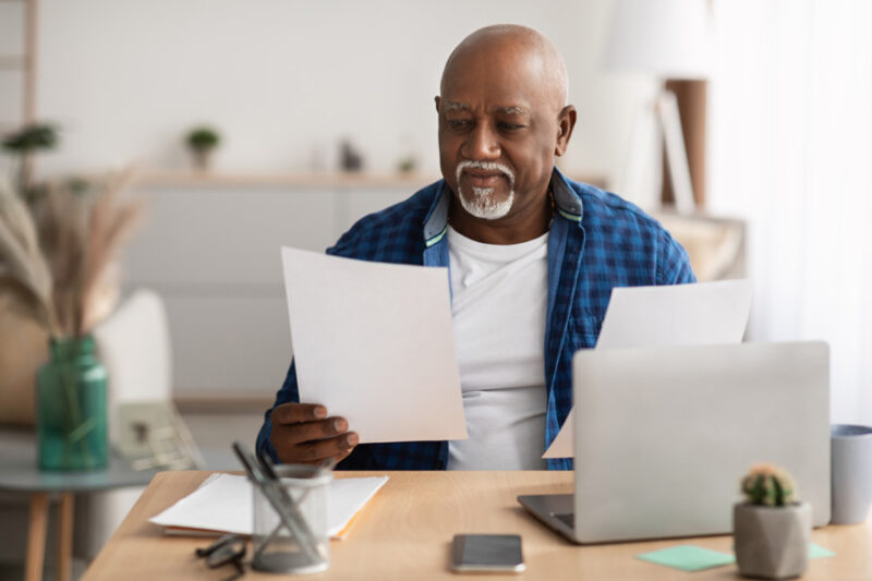 Mature Black Businessman Working With Papers Sitting At Laptop In Modern Office.