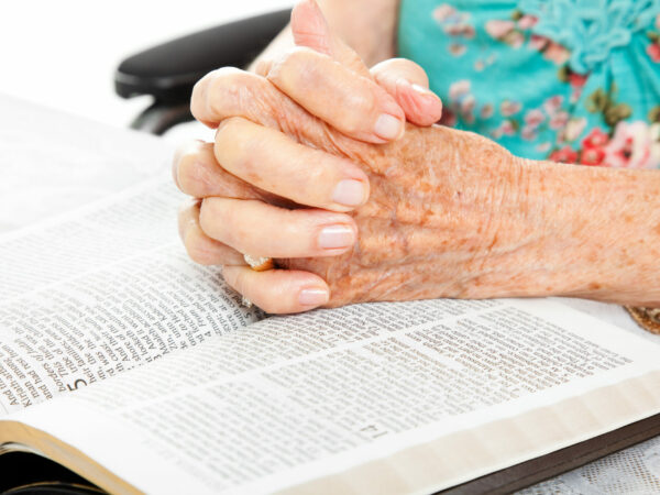 Hands folded in prayer and resting on a Bible.