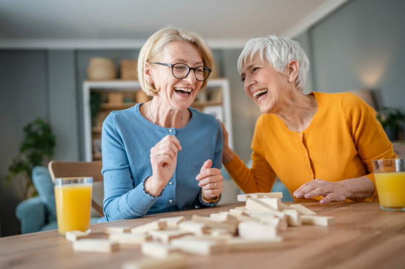 two senior women female woman friends or family sisters play leisure board game at home.